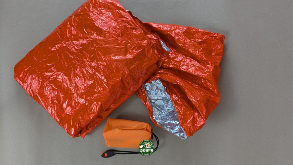 Folded orange mylar emergency poncho with silver interior and whistle bag on kraft paper